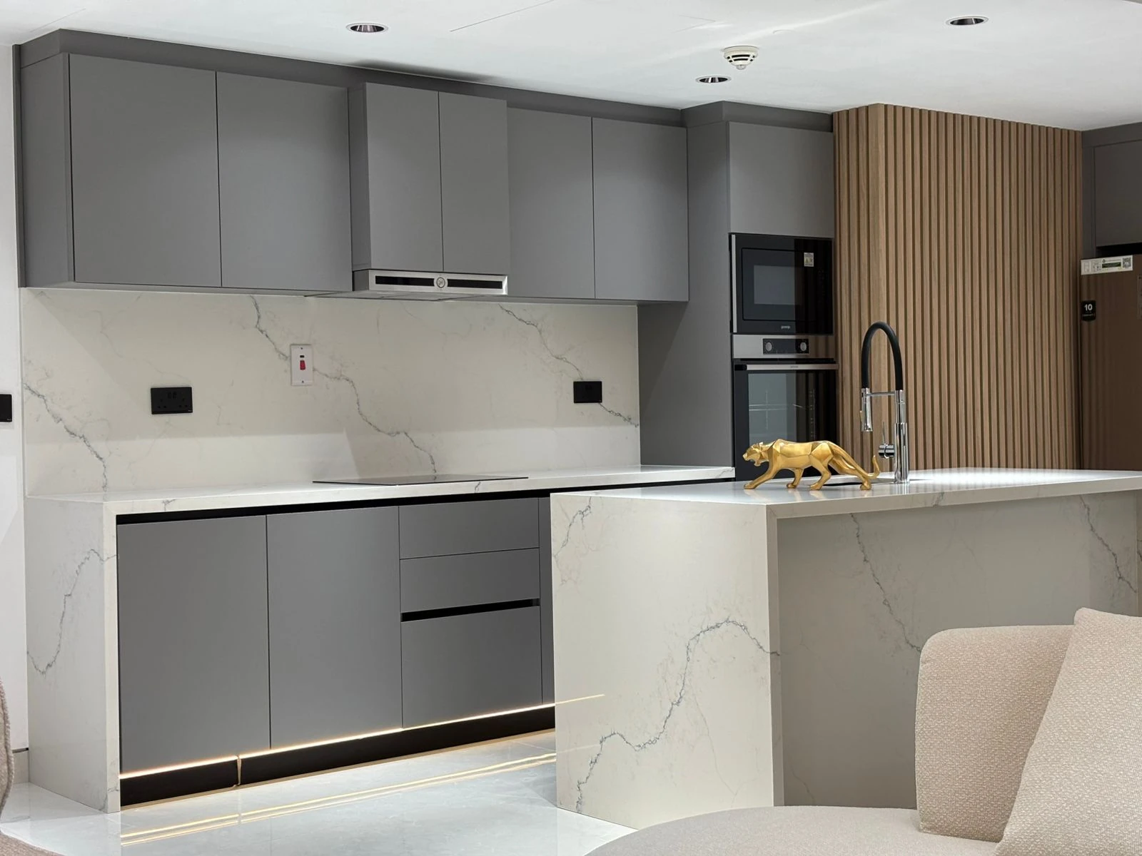 Completed kitchen with grey cabinetry, stone worktops and timber slatted wall